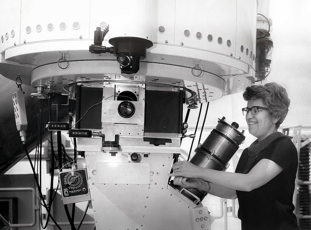 Foto von Vera Rubin im Kitt Peak National Observatory im Jahr 1963 bei der Bedienung des Teleskops Nr. 1 des Observatoriums. 36-Zoll-Teleskop. Der Bildröhrenspektrograph von Kent Ford ist am Teleskop befestigt. Zusammen mit Ford benutzte sie weiterhin das Kitt Peak 2.1-m-Teleskop und sammelte in den folgenden Jahren über 60 Galaxienrotationskurven. Flache Rotationskurven waren direkt aus den Spektren ersichtlich: Diese Daten lieferten überzeugende Beobachtungsnachweise für eine neue Art von Materie im Universum, die 'dunkle Materie'. Vera Rubin setzte ihre Beobachtungen am Kitt Peak und am Cerro Tololo während ihrer langen Karriere fort.