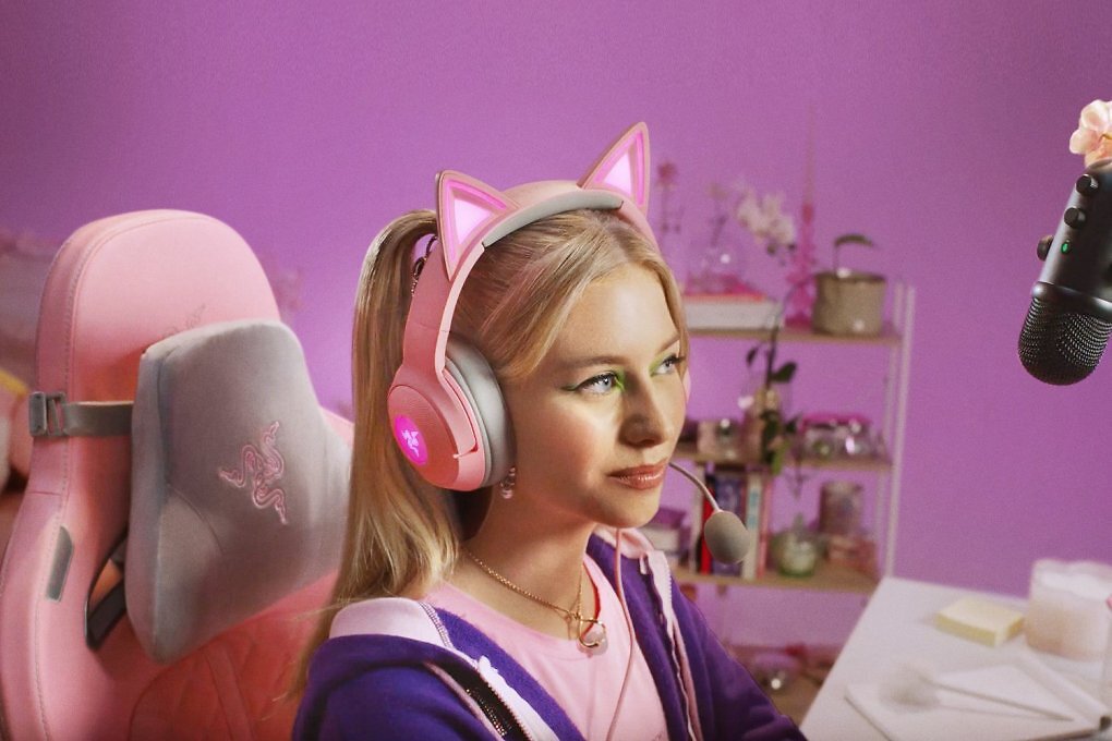 EIne Frau mit blonden Haaren trägt ein rosafarbenes Razer-Headset, das obendrauf Katzenöhrchen hat.