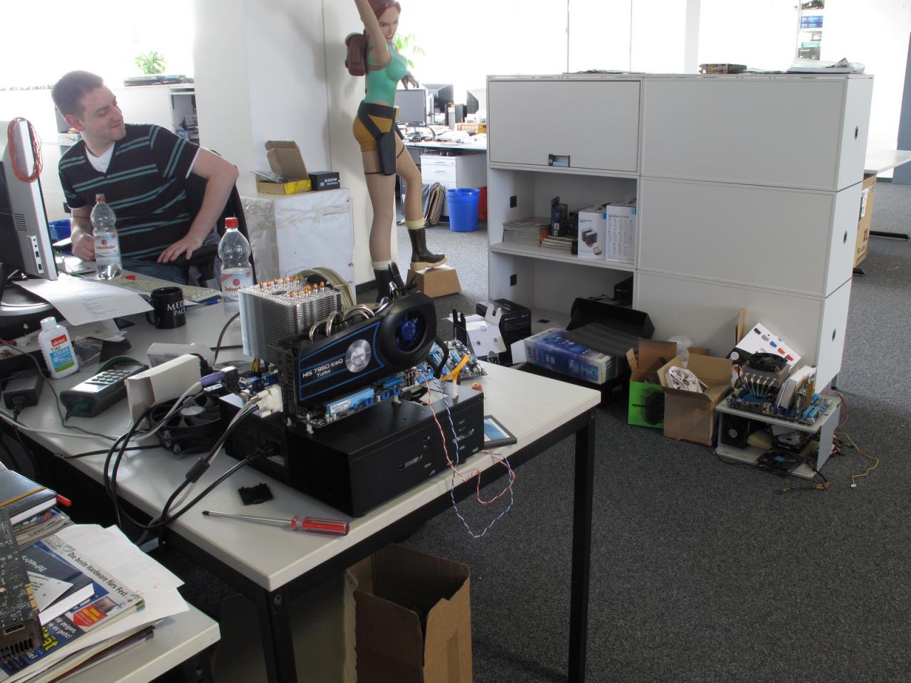 [18/05/2012] Wo gehobelt wird, fallen bekanntlich auch Späne oder es sammelt sich wie im Fall von Signore Staudacher auch einiges an Lüftern inklusive Verpackung sowie Benchtables/Testsysteme rund um den Arbeitsplatz an. An Reinhards Blick erkennt man zumindest, dass er sich freut, die Kühlertests endlich hinter sich gebracht zu haben. 