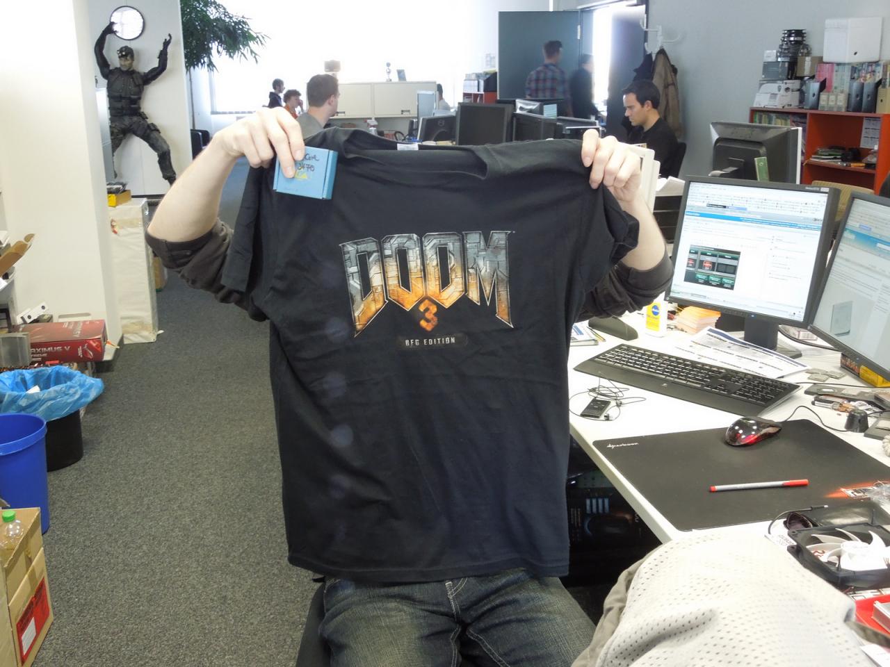 [19/10/2012] Auch diesen Redakteur hat es erwischt. Oder haben wir ihm etwa nur das Shirt, das vorher sein Kollege Raff anhatte, sprichwörtlich in die Hände gedrückt? Raten Sie doch einfach mal! Und wer sich nicht sicher ist, bei wem das Doom 3 BFG-Shirt gelandet ist, spätestens der nur notdürftig verpackte Prozessor in seiner rechten Hand sollte diesen Redakteur entlarven. 