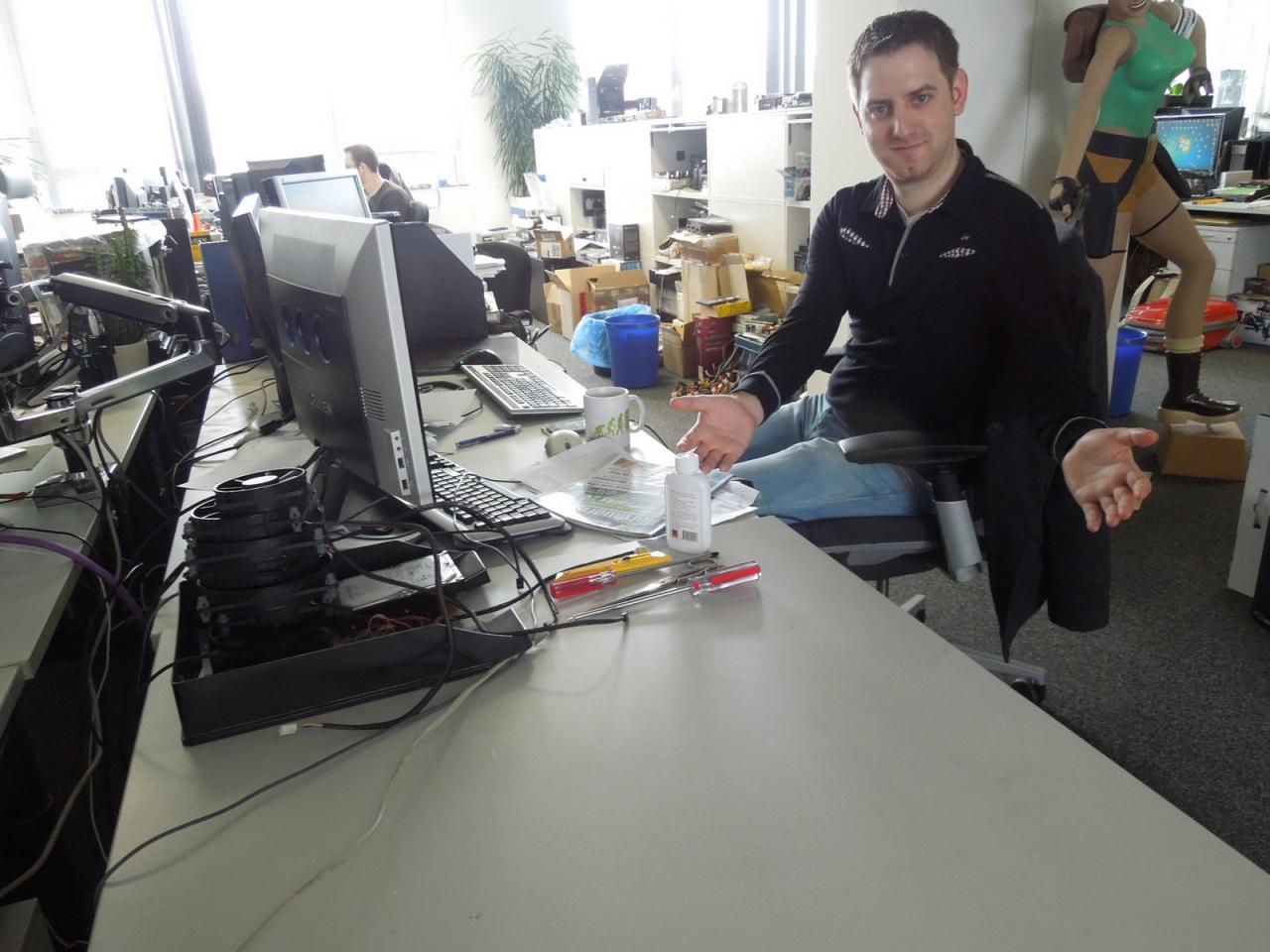 [24/05/2013] Dieses Bild hat eher Seltenheitswert. Steinhard, der diese Woche schon fleißig für das Pad & Phone-Sonderheft tippte, hat seinen Schreibtisch nicht nur aufgeräumt, sondern förmlich leer gefegt. Und wie man der Geste von Herrn Staudacher entnehmen kann, präsentiert er dieses Wunder sehr gern, denn er hat auch nicht getrickst und seine CPU-Lüfte-Kollektion einfach unter dem Schreibtisch verstaut.
