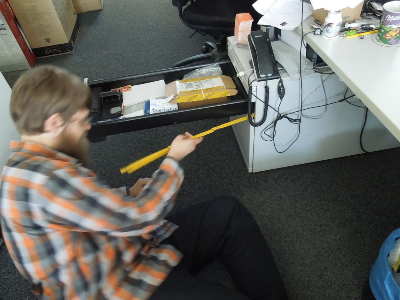[29/08/2014] Hier sehen Sie Stephan, wie er mit einem Zollstock in seinem Schrank herumstochert. Auf Nachfrage versicherte er uns, dass es hierbei nur darum gehen würde, eine blockierte Schublade zu reparieren. Da der baugleiche Schrank vom Kollegen nebenan ein reichhaltiges Angebot von SSDs bereithält, liegt aber die Vermutung nicht fern, dass diese Versuche als Probeläufe für einen Italian Job beim italienischen Kollegen dienen.