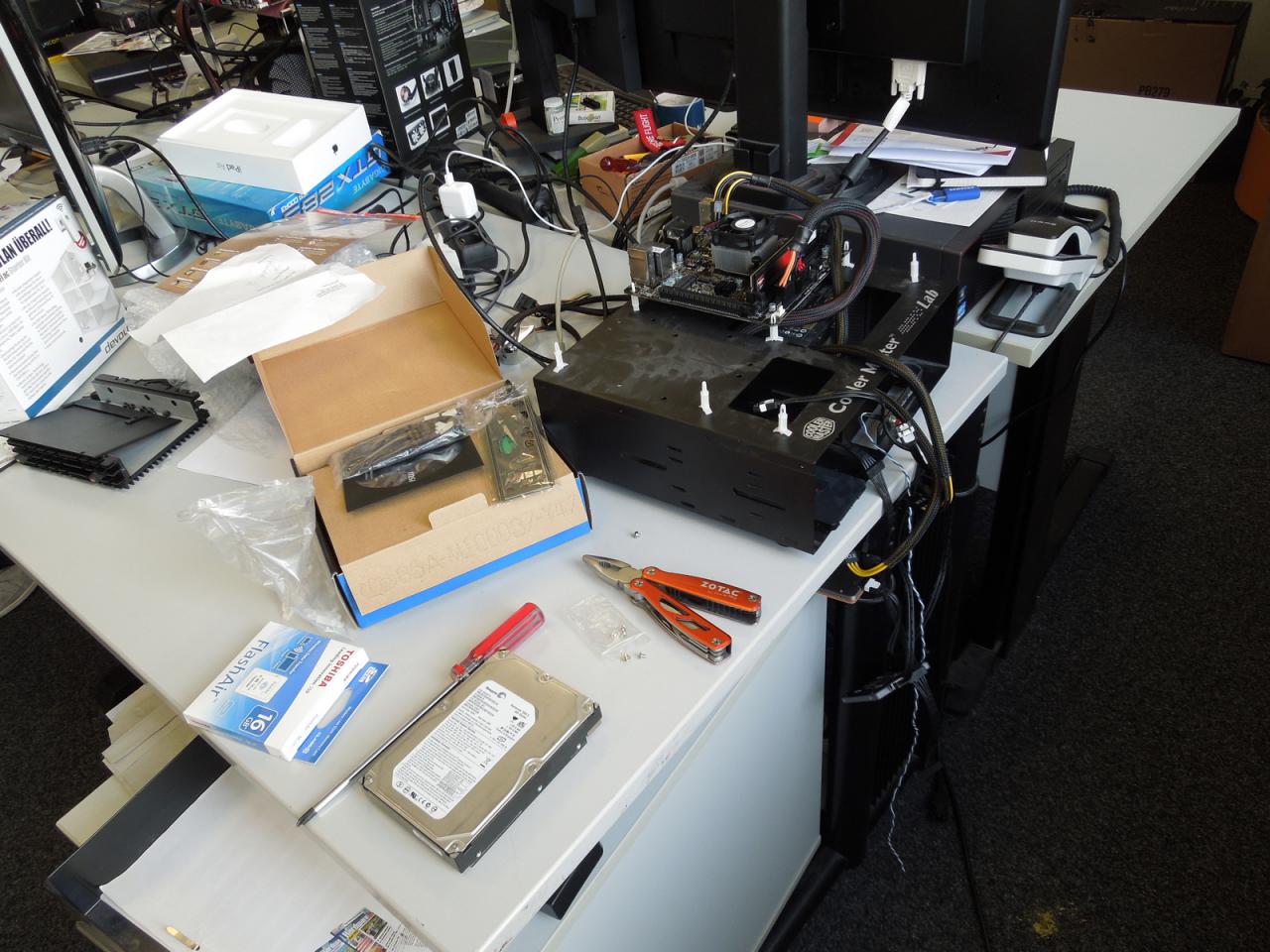 [21/11/2014] Gerade in der Abgabewoche lohnt sich schon einmal ein Bilderrätsel wie dieses, bei dem wir fragen, welchem Kollegen denn dieser Schreibtisch sowie das Testsystem mit der Mini-Platine und dem süßen kleinen CPU-Kühler wohl gehört. Die Tatsache, dass hier nicht aufgeräumt ist, kann in der finalen Produktionswoche jedenfalls nicht wirklich als Hinweis gedeutet werden und 