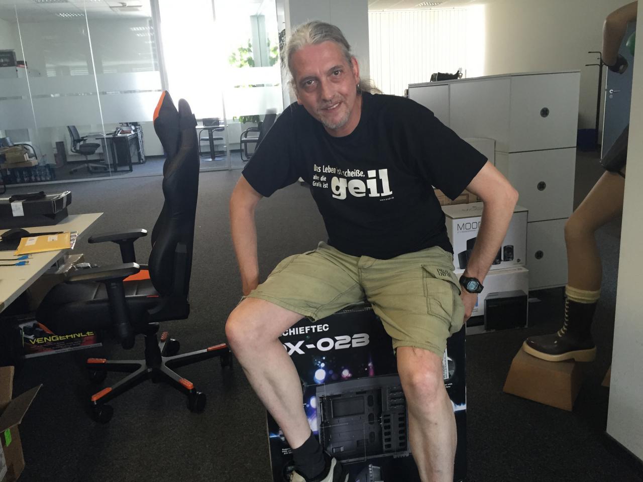 [14/08/2015] 16.8.2015: So ruhig und relaxed, wie unser Redaktions-Dino hier auf dem Bild wirkt, war er in den vergangenen Arbeitstagen nur selten. Noch nimmt er es locker und ruht sich ein bisschen auf dem nicht ganz ungemütlichen Gehäusekarton aus. Wenn's dagegen ans Auspacken und Testen geht, könnte es in Abhängigkeit zur Güte des Gehäuse-Testmusters schnell wieder laut werden. Allerdings dürfen Sie auf diesem Bild eine ganz andere Premiere bestaunen. Die sommerliche Hitze zwang selbst den Tastaturpapst dazu, mit kurzer Hose aufzulaufen. Und von dem netten älteren Herrn gab es bisher keinen Bildbeweis mit einem kurzen Beinkleid.