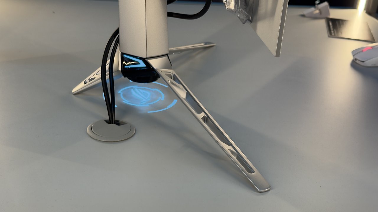 [19/08/2025] Detailaufnahme des silbernen Standfußes des ROG Swift OLED mit ROG-Logo-Projektion.