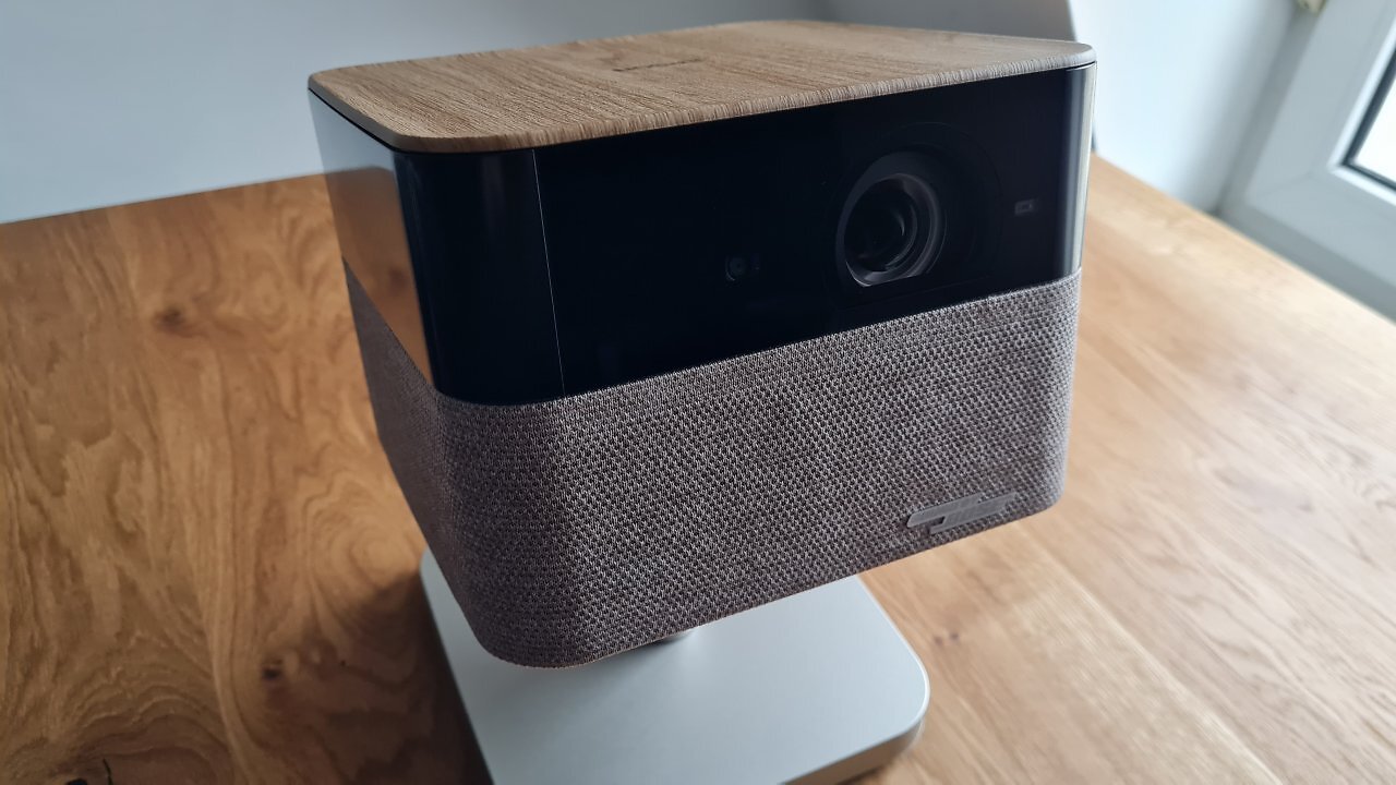 Ein viereckiger Beamer mit Standfuß auf einem Holztisch