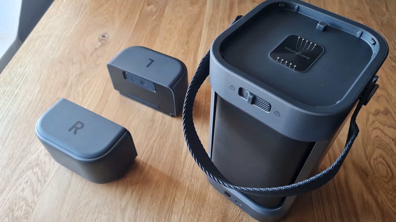 Ein tragbarer Mini-Beamer samt Lautsprecherboxen auf einem Holztisch.