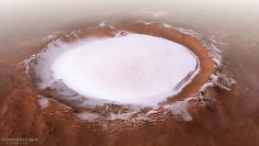 Dieses Bild von der Mars Express der ESA zeigt den Korolev-Krater, ein 82 Kilometer großes Merkmal in den nördlichen Tiefebenen des Mars. –Diese schräge Perspektivenansicht wurde mithilfe eines digitalen Geländemodells und Daten der Mars Express generiert, die über die Umläufe 18042 (aufgenommen am 4. April 2018), 5726, 5692, 5654 und 1412 gesammelt wurden. Der Krater selbst befindet sich auf der Marsoberfläche bei 165° E, 73° N. Die Bildauflösung beträgt ungefähr 21 Meter pro Pixel. – Dieses Bild wurde unter Verwendung von Daten aus den Nadir- und Farbkanälen der High Resolution Stereo Camera (HRSC) erstellt. Der Nadir-Kanal ist senkrecht zur Marsoberfläche ausgerichtet, als ob er direkt auf die Oberfläche schauen würde.