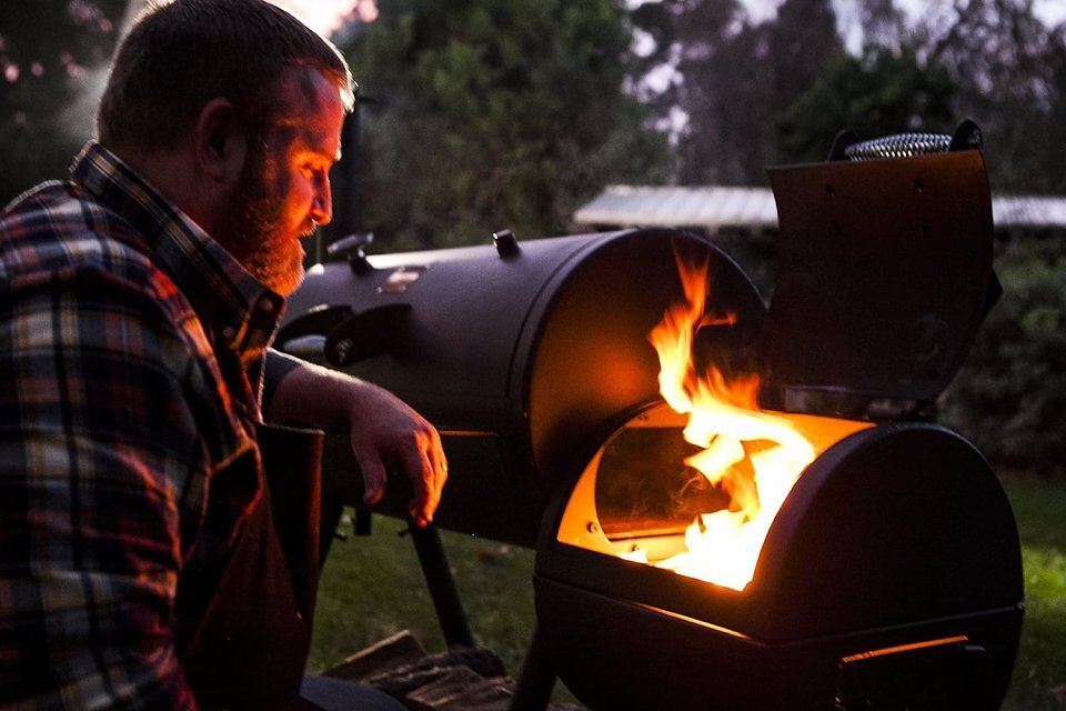 Ein Mann, der vor einem Grill sitzt, aus dem die Flammen aufsteigen