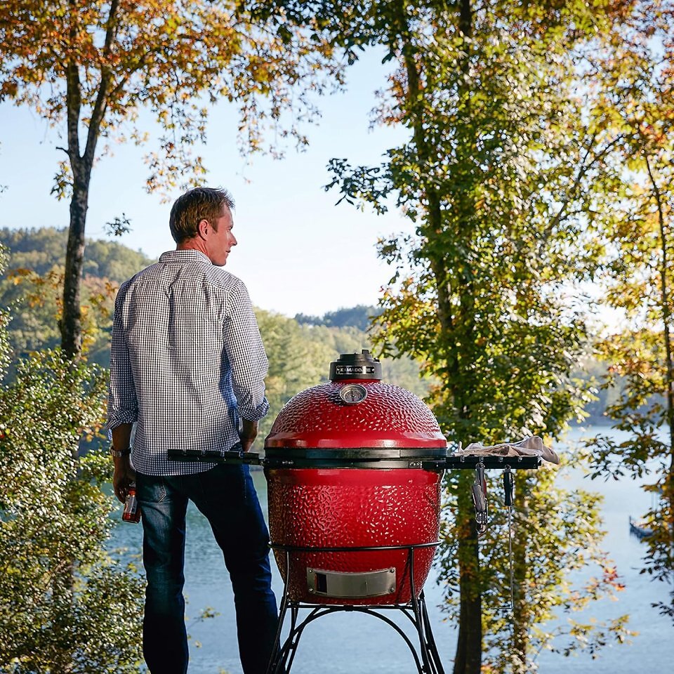 Ein Mann steht neben einem Grill vor einem See