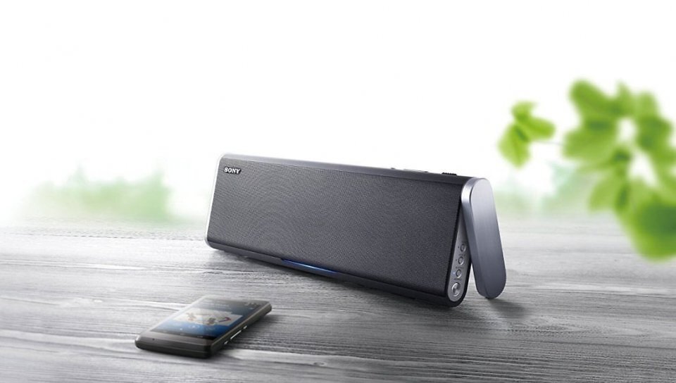 Der Sony-Bluetooth-Lautsprecher s-l1600 auf einem Tisch stehend. Davor liegt ein Handy.