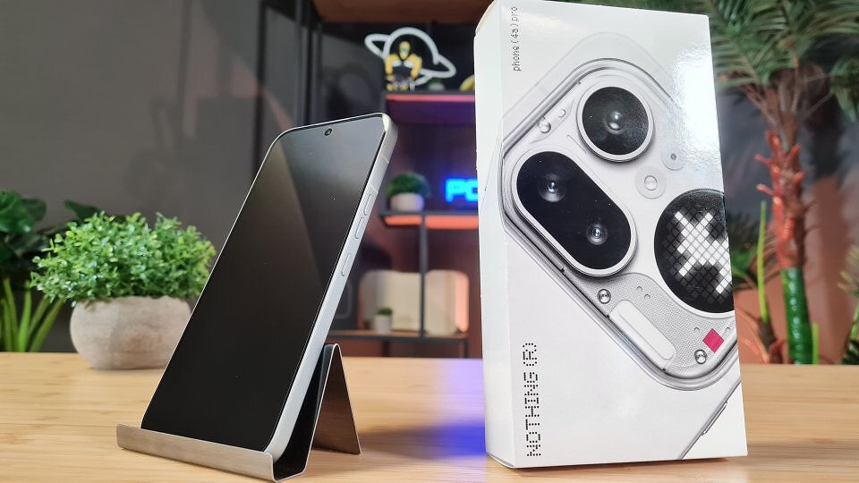 Ein Smartphone steht neben der Packung auf einem Holztisch