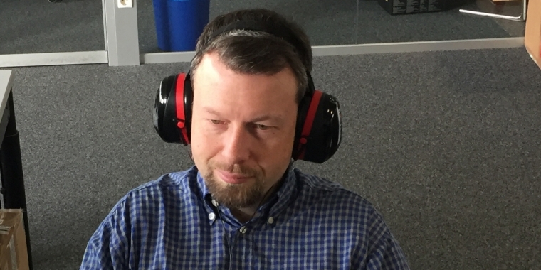 Sie erinnern sich sicher an die diversen Bilder von Herrn Doktor Spille, wenn der sich im sogenannten Abgabemodus befindet. Er erzählt uns dann immer, er trage den Kopfhörer dann nur, um sich bei harter Metal-Musik zu entspannen. Dass dieser Akt allerdings eine akustische Schutzmaßnahme gegen das unüberhörbare Tippen der Kollegen Reuther und Stöwer auf ihren mechanischen Tastaturen ist, hat Carsten nur indirekt angedeutet. Doch irgendwann war das Maß voll und die Klänge kräftiger Gitarren sowie eine Double-Bass-Kanonade helfen auch in der Abgabewoche nicht mehr. Der 3M-Peltor-Optime-III-Gehörschutz musste her und erst der lässt nur noch seine geliebte Musik, nicht aber das Klackern der Keyboardtasten an Carstens Gehörgang dringen. Herr Spille ist aber auch ein pfiffiges Kerlchen :)